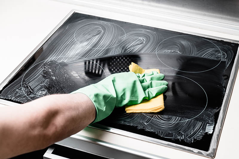 Man's hand in green glove cleaning cooker at home kitchen